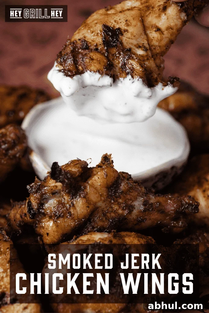 Smoked jerk chicken wing dipped in ranch surrounded by a pile of chicken wings.