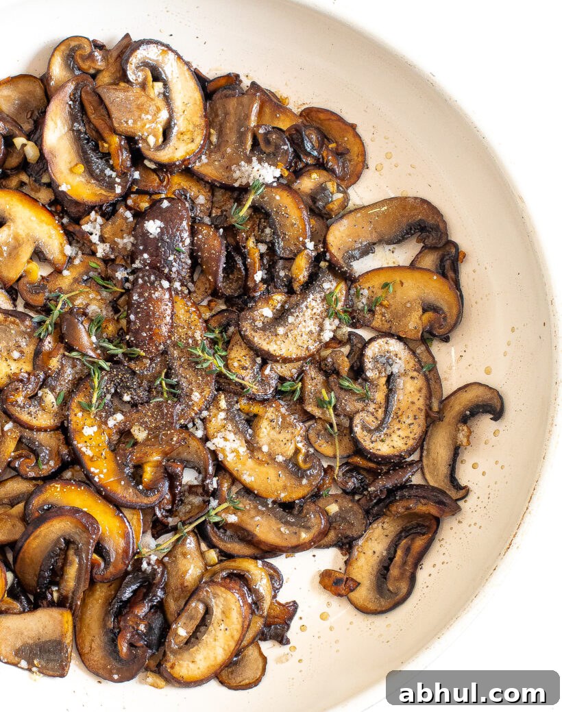 Overhead shot of sauteed mushrooms in a skillet topped with salt and thyme. 
