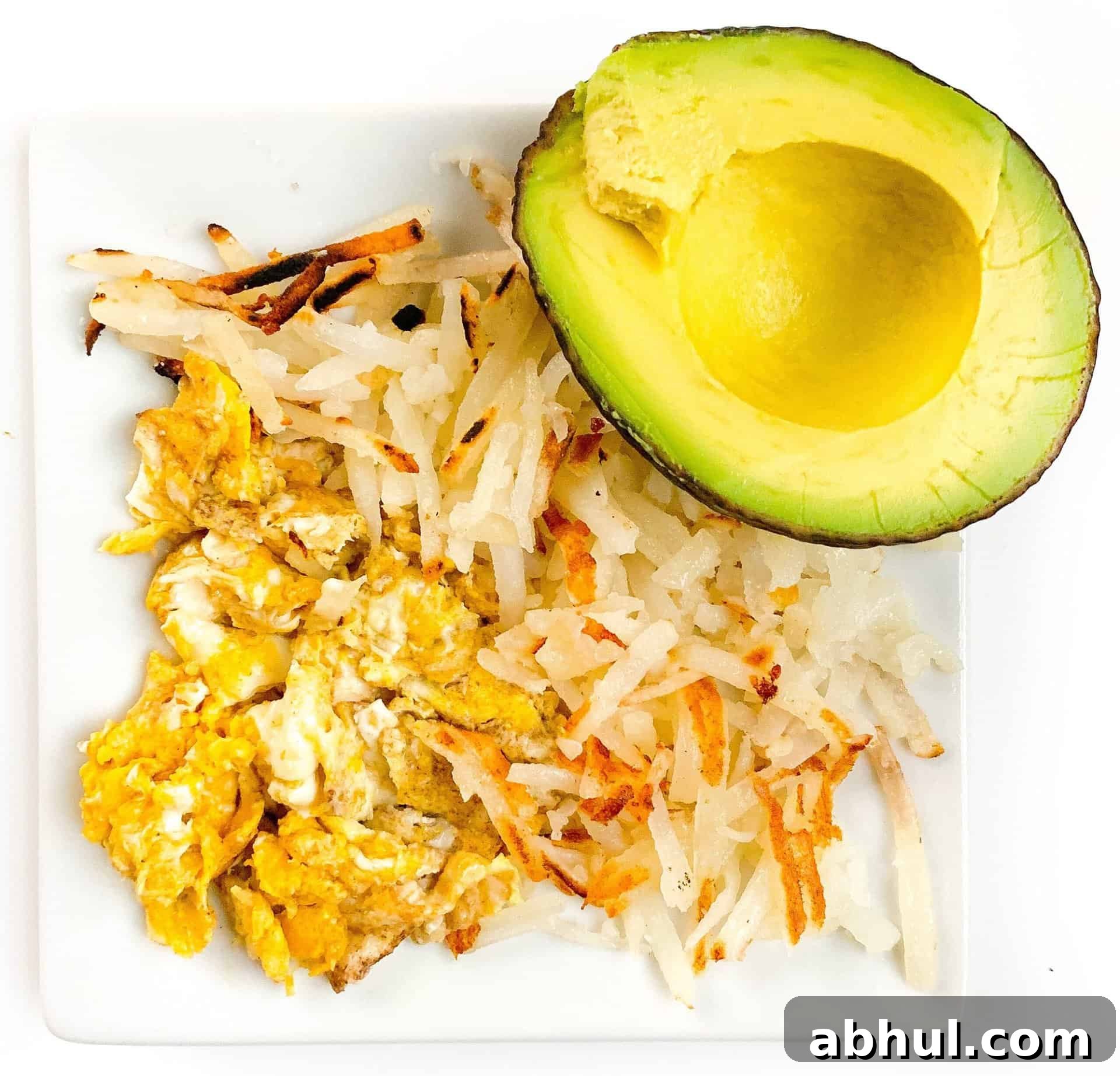 scrambled eggs, hash brown potatoes, and avocado on a white plate for a one year old breakfast