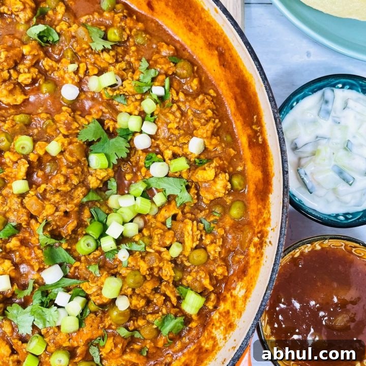 Image shows chicken keema in a pan besides some bowls of poppadoms, mint sauce, mango chutney, and rice