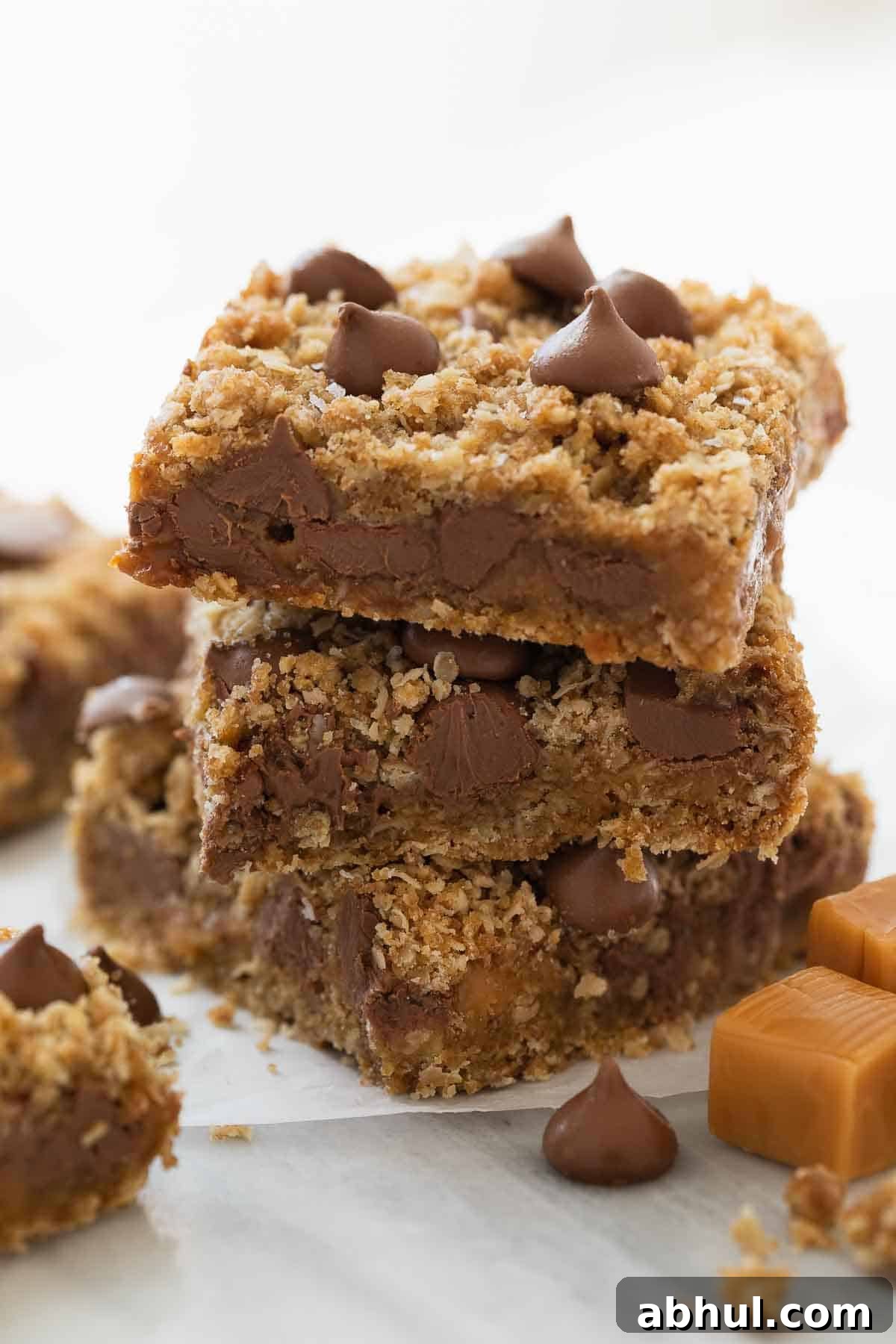 Gluten-Free Seven-Layer Bars Recipe — Chewy Chocolate Coconut Bars 14 stack of gluten free oatmeal cookie bars with chocolate and caramel on white marble background