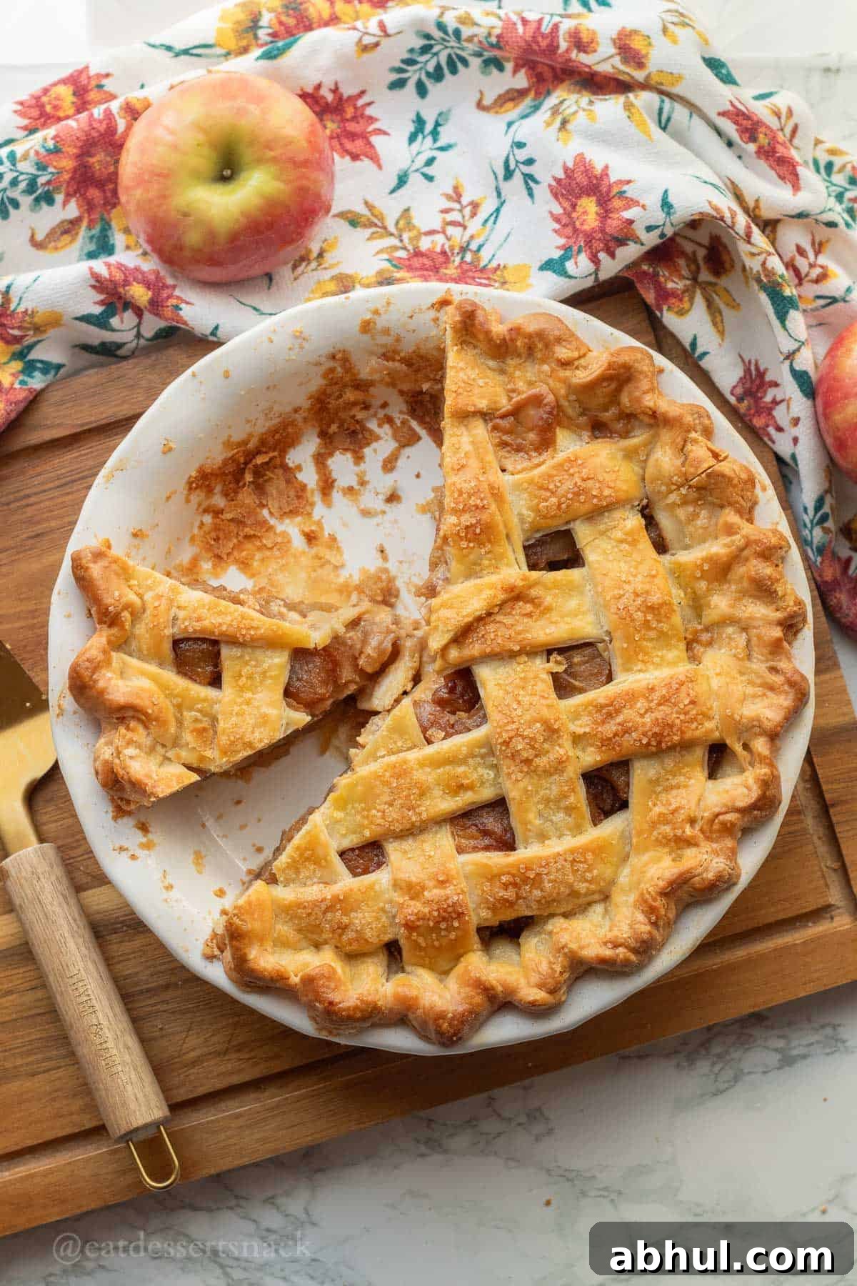 Baked caramel apple pie in white pie dish on wood cutting board.