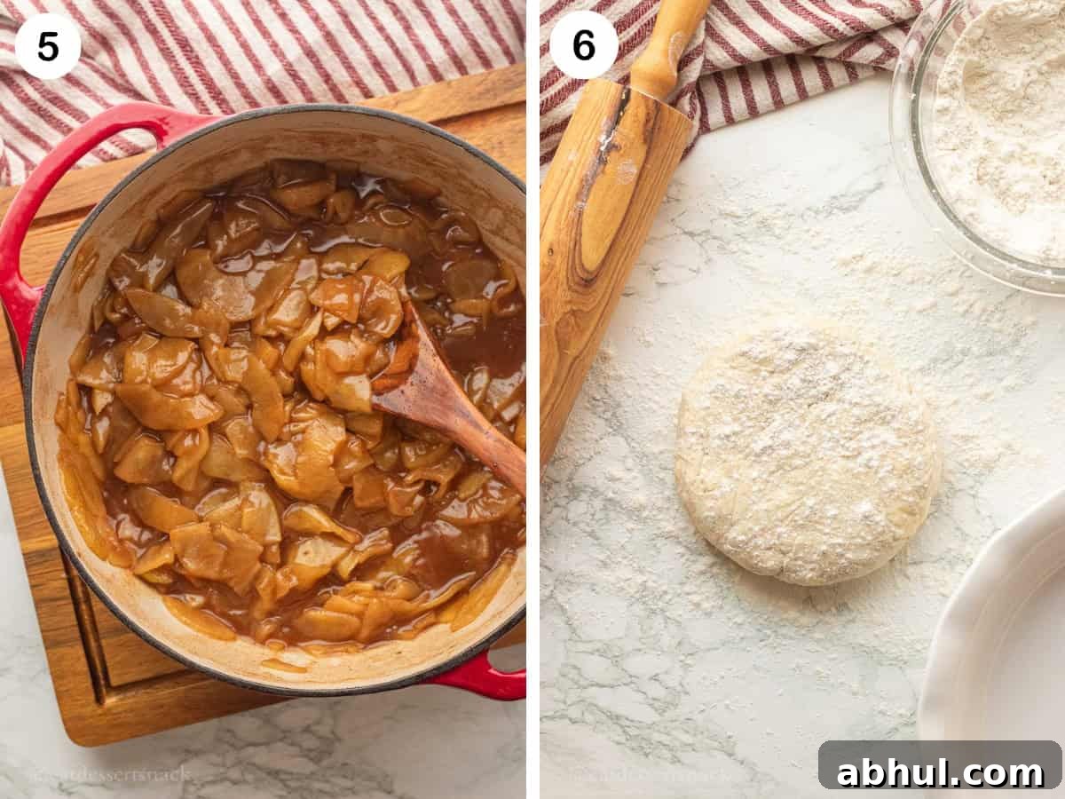 Cooked apple pie filling in red pot and raw pie dough disc with flour on marble surface.