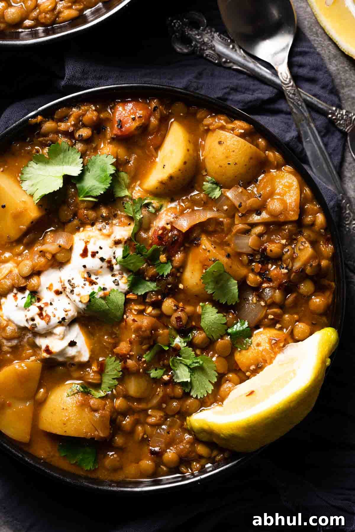 lentil potato soup in black bowl with lemon wedge garnish
