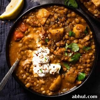 lentil potato soup in bowl with spoon in bowl and lemon wedge on the side