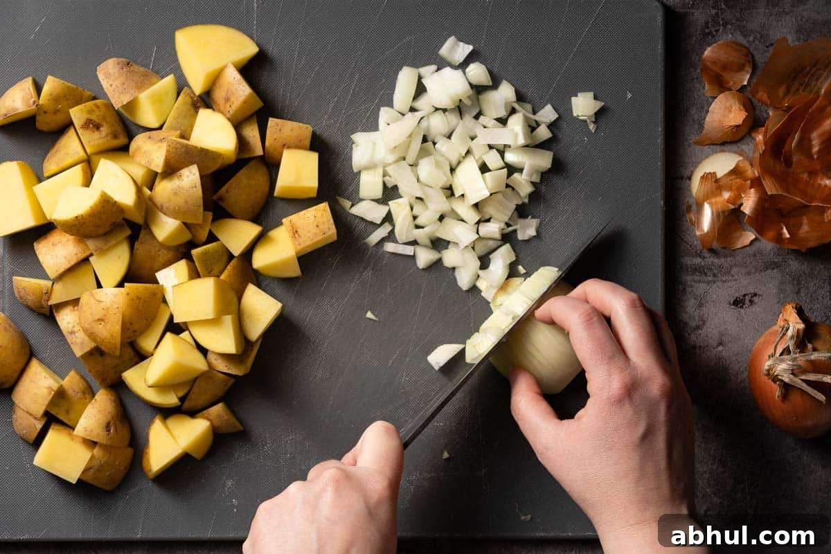 onion being chopped on cutting board with chunks of potatoes on the side