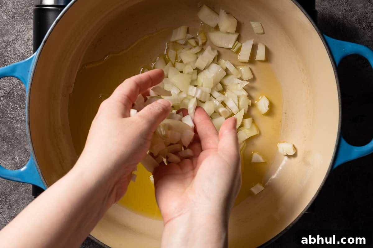 hands adding chopped onion into pot with oil