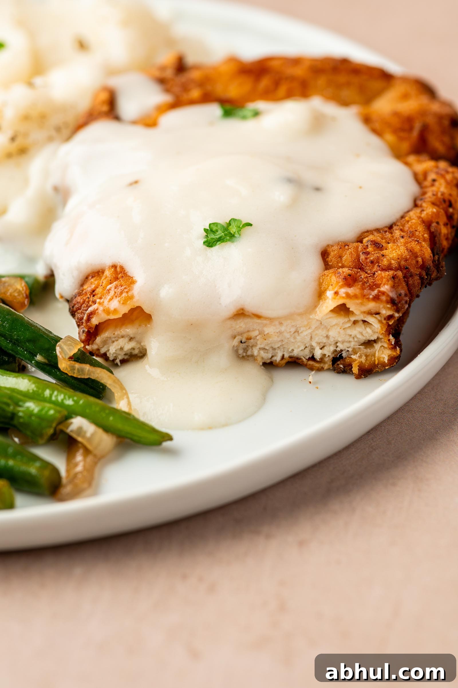 Crispy Chicken-Fried Chicken with Classic White Gravy 7 A plate of chicken fried chicken topped with white gravy, served with mashed potatoes and green beans.