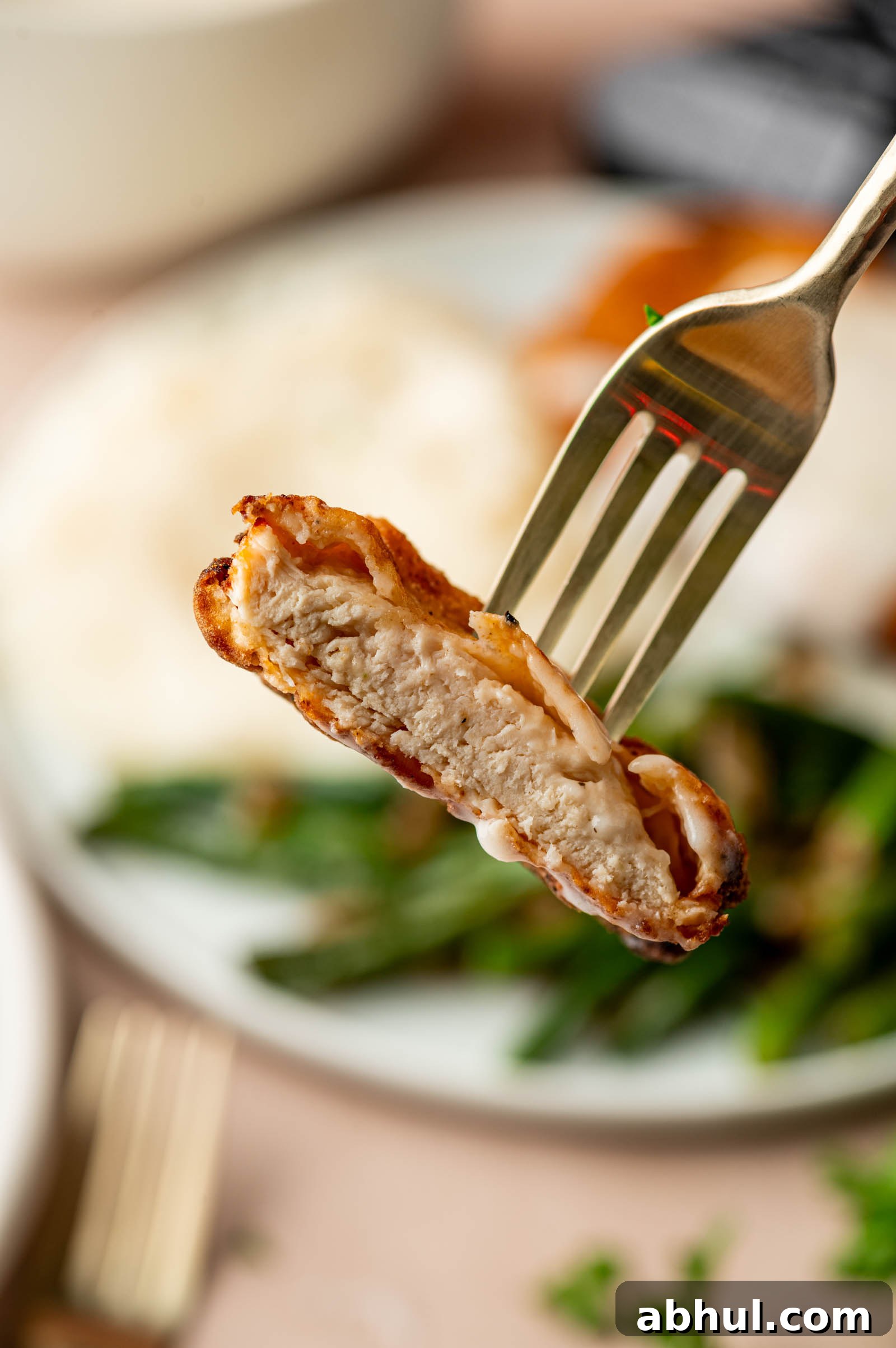 Crispy Chicken-Fried Chicken with Classic White Gravy 5 A fork holds a bite of cooked, chicken fried chicken with crispy fry coating and gravy, with green beans and potatoes blurred in the background on a plate.