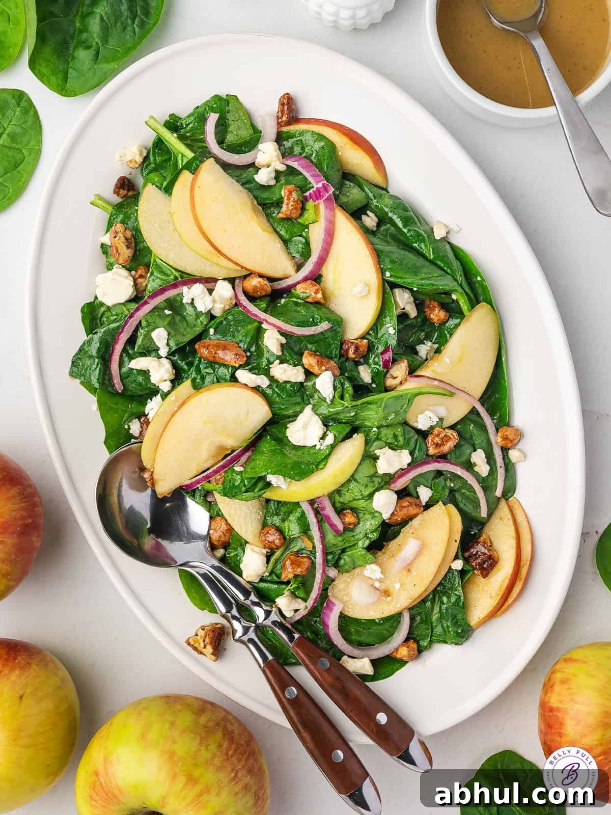 Baby spinach, apples, candied pecans, and goat cheese are tossed with a simple homemade vinaigrette in this Spinach Apple Salad. Overhead view of a spinach apple salad on a white platter