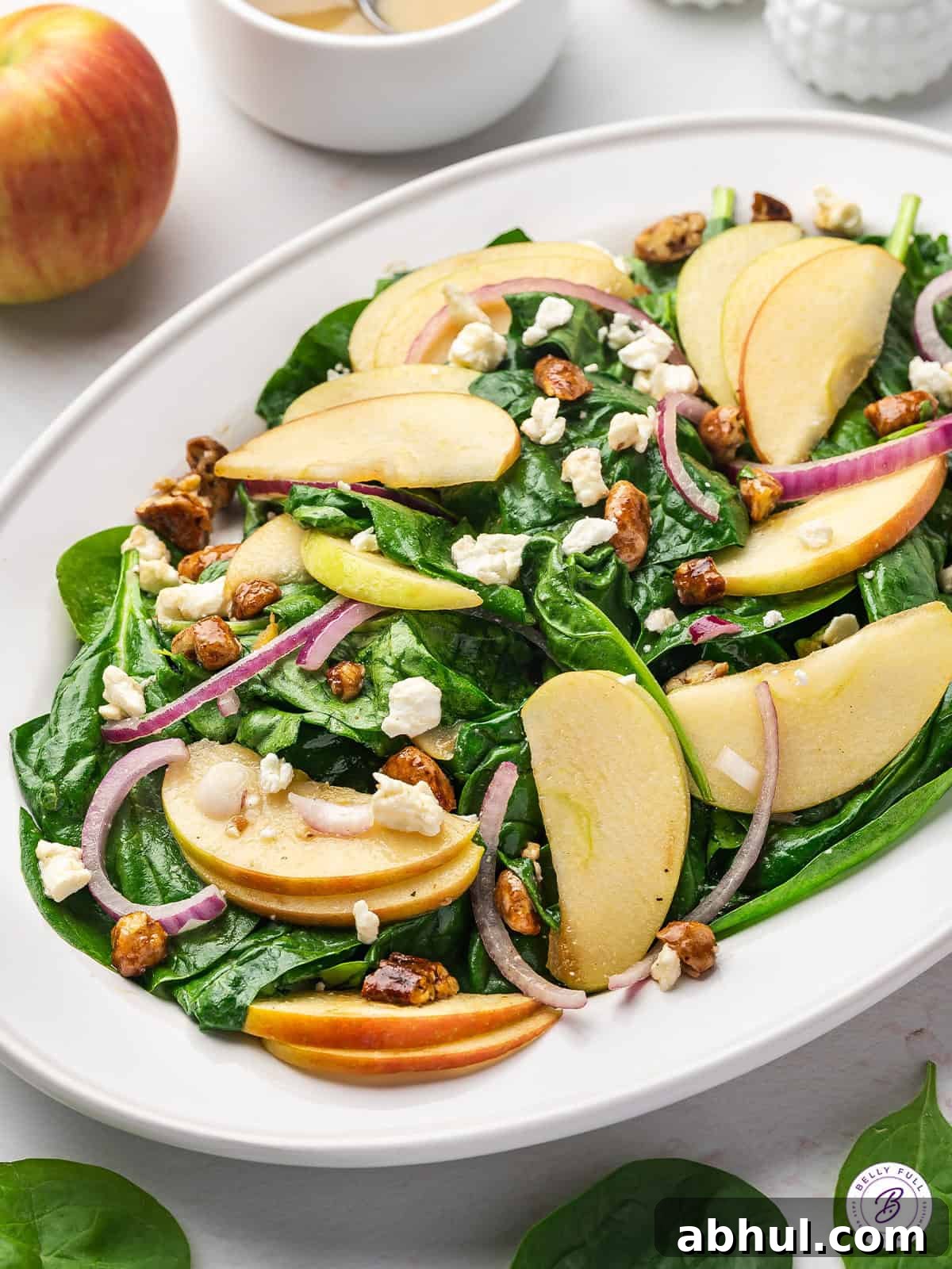 Baby spinach, apples, candied pecans, and goat cheese are tossed with a simple homemade vinaigrette in this Spinach Apple Salad. A spinach apple salad on a white platter