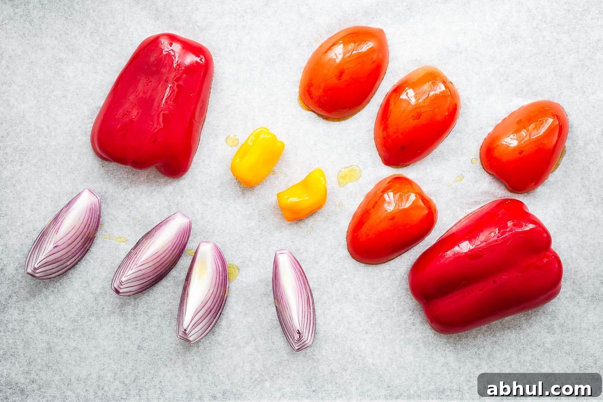A parchment-lined baking sheet with bell pepper, red onion wedges, tomatoes and habanero peppers for roasting.