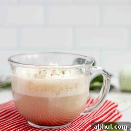 side view of a eggnog latte topped with whipped cream and sprinkles in a glass mug on a red towel on a marble countertop surrounded by sprinkles and greenery.