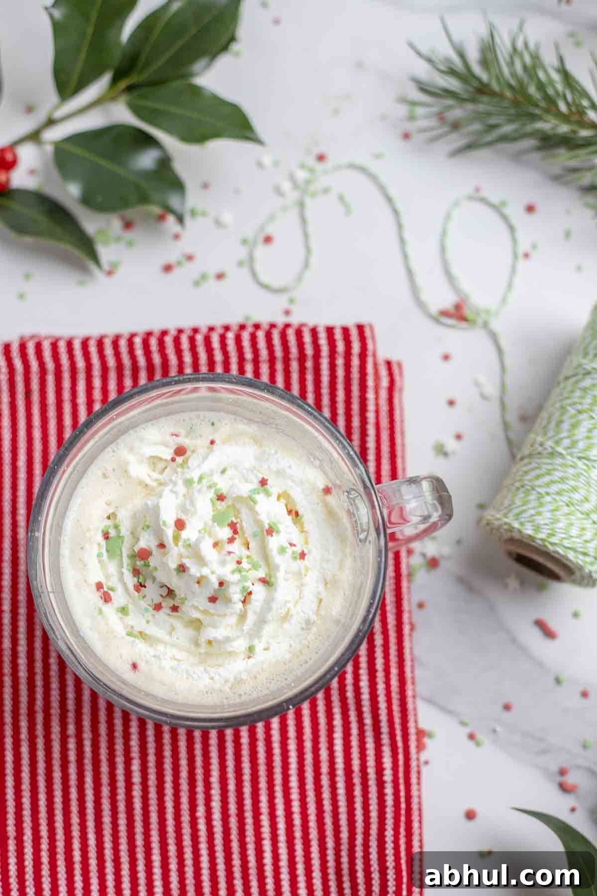 eggnog latte topped with whipped cream and sprinkles on a red stripped towel.