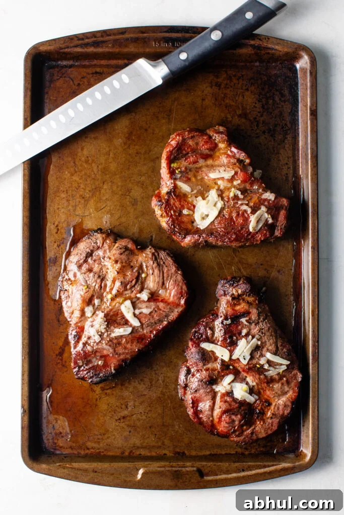 grilled pork coppa steaks topped with garlic on a sheet pan