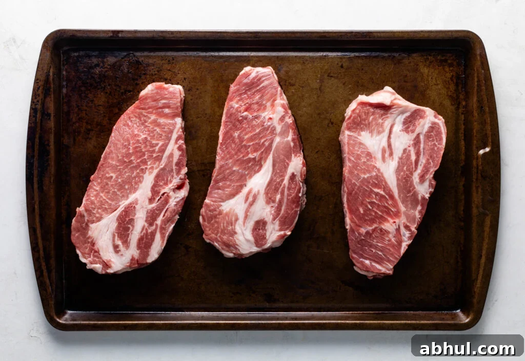 three raw pork coppa steaks on a sheet pan