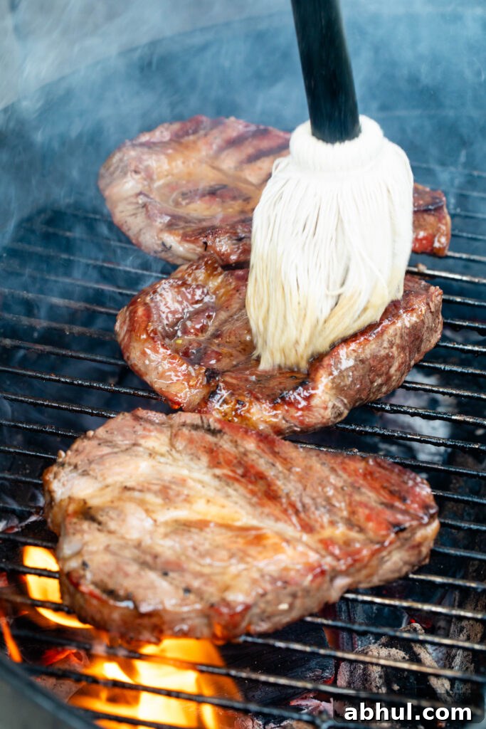 basting pork coppa steaks on the grill over lit coals.