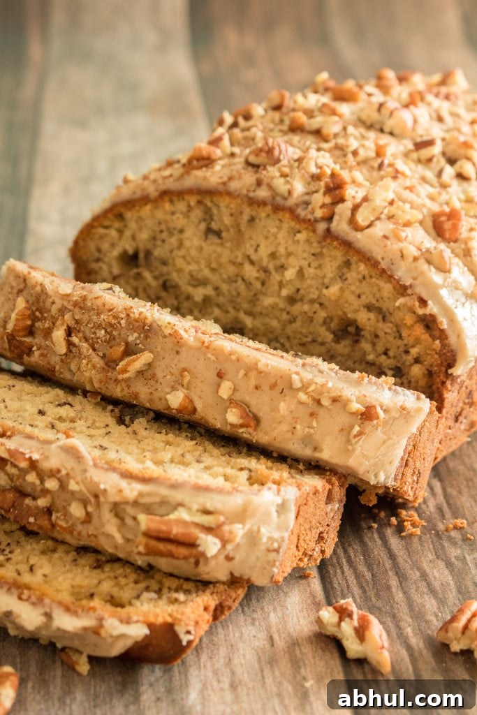 partially sliced loaf of gluten free banana bread topped with glaze and chopped pecans