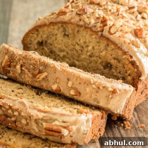 a loaf of gluten free banana bread partially sliced. It has a light brown glaze and chopped pecans on top