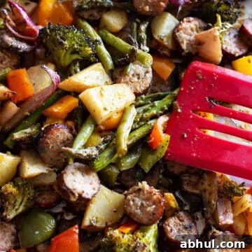 Sheet Pan Sausage with Roasted Vegetables Recipe 15 Person serving sausage and vegetables from a sheet pan for dinner.