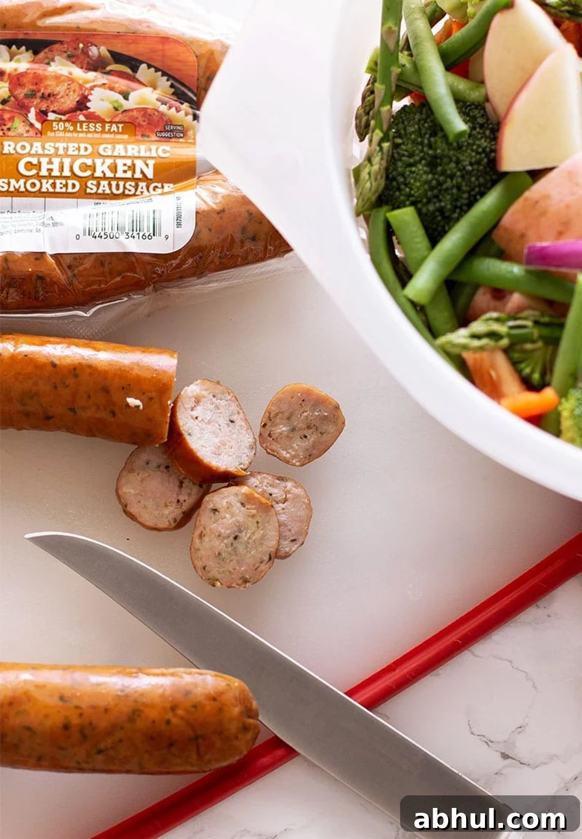 Sheet Pan Sausage with Roasted Vegetables Recipe 5 Knife slicing smoked sausage on a cutting board.