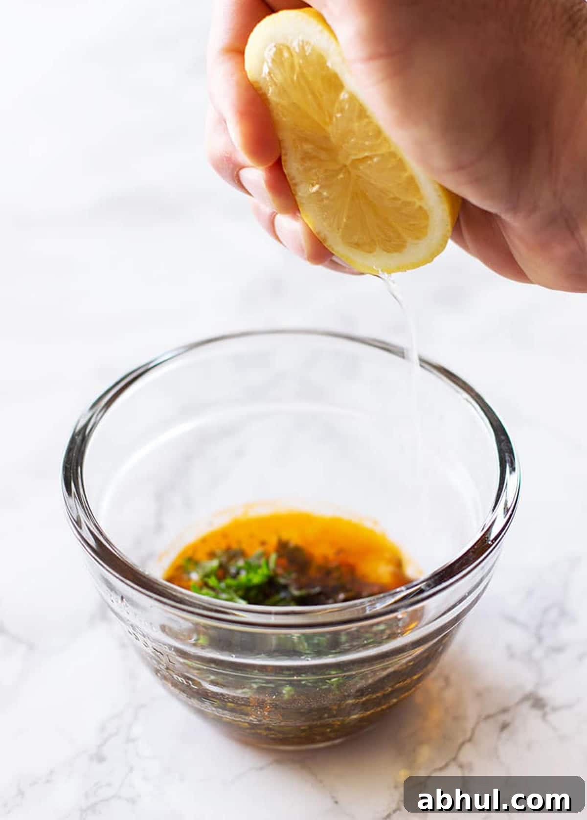 Sheet Pan Sausage with Roasted Vegetables Recipe 6 Hand squeezing a lemon into a bowl to make a marinade.