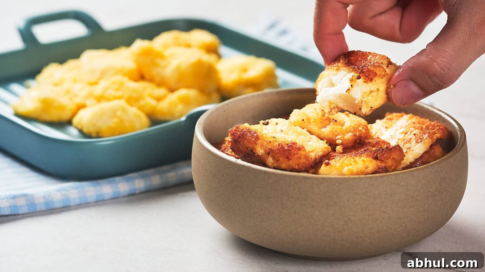 A hand picks up a piece of fried cheese curd from a bowl.