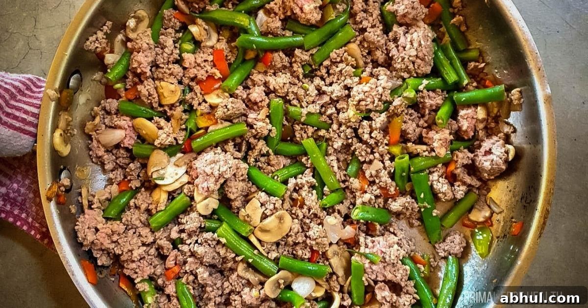 A picture of ground beef and green bean stir-fry in stainless steel skillet.