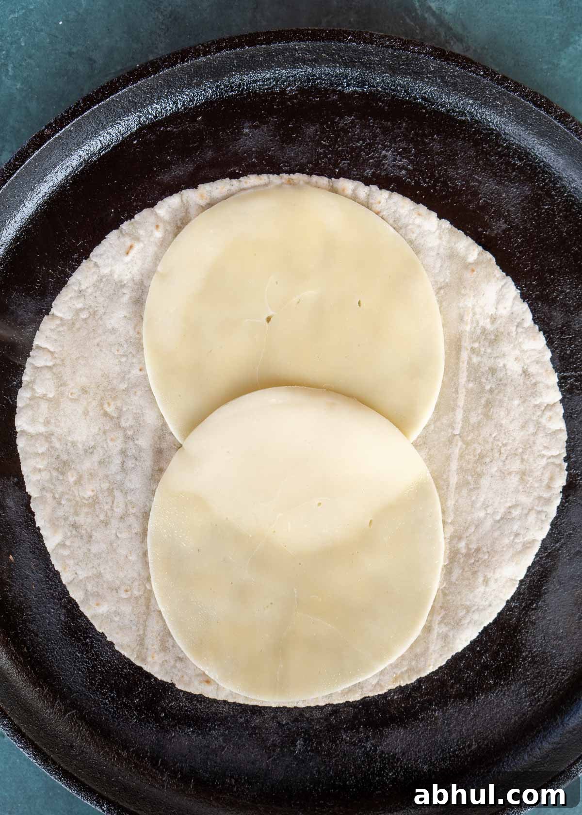 Philly Cheesesteak Wrap Recipe: Quick Steak & Cheese Wraps 6 a tortilla warming on a skillet with two slices of provolone for an easy steak wrap