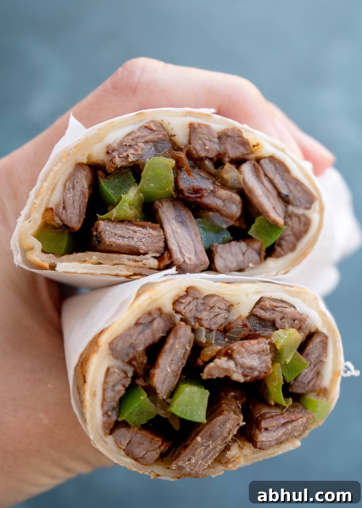 Philly Cheesesteak Wrap Recipe: Quick Steak & Cheese Wraps 9 a hand holding two meaty philly cheesesteak wraps full of sirloin, peppers, and onions