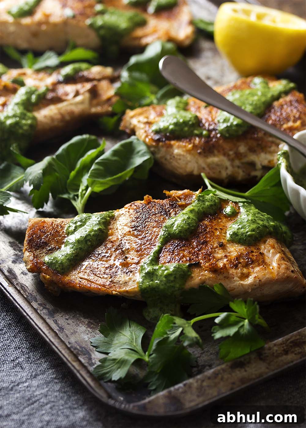 Golden brown salmon fillets on a tray drizzled with green sauce.