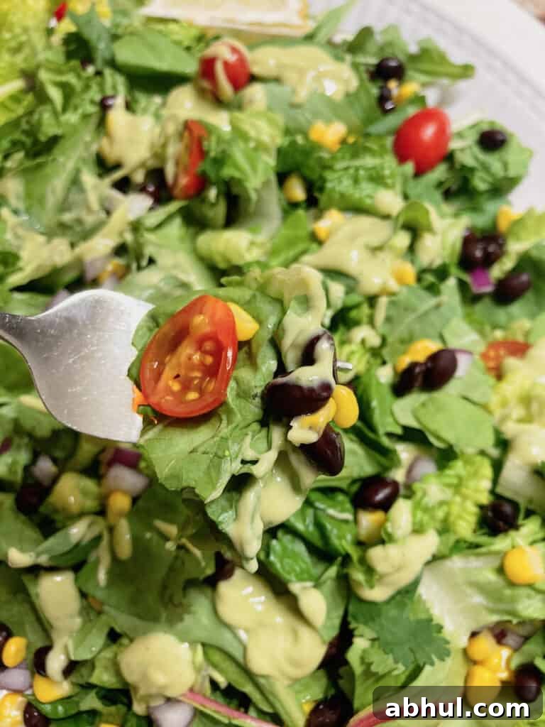 mixed greens, tomato, black beans and avocado dressing on a fork.