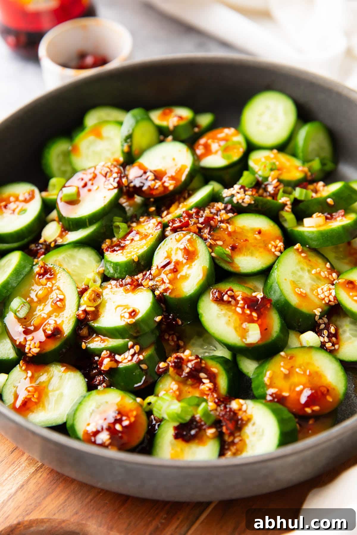 Asian cucumber salad served in a large rimmed dish topped with spicy dressing.