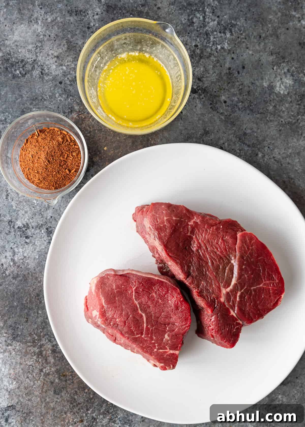 overhead: blackened steak seasoning, melted butter, and beef tenderloin on a white plate