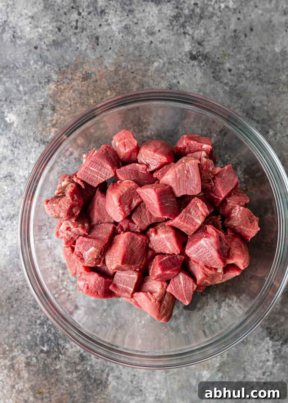 overhead process shot: cubed raw beef in a glass bowl