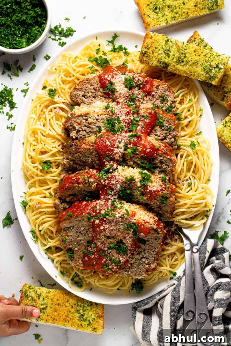 Large white platter with an Italian meatloaf sliced on top of a bed of spaghetti noodles 