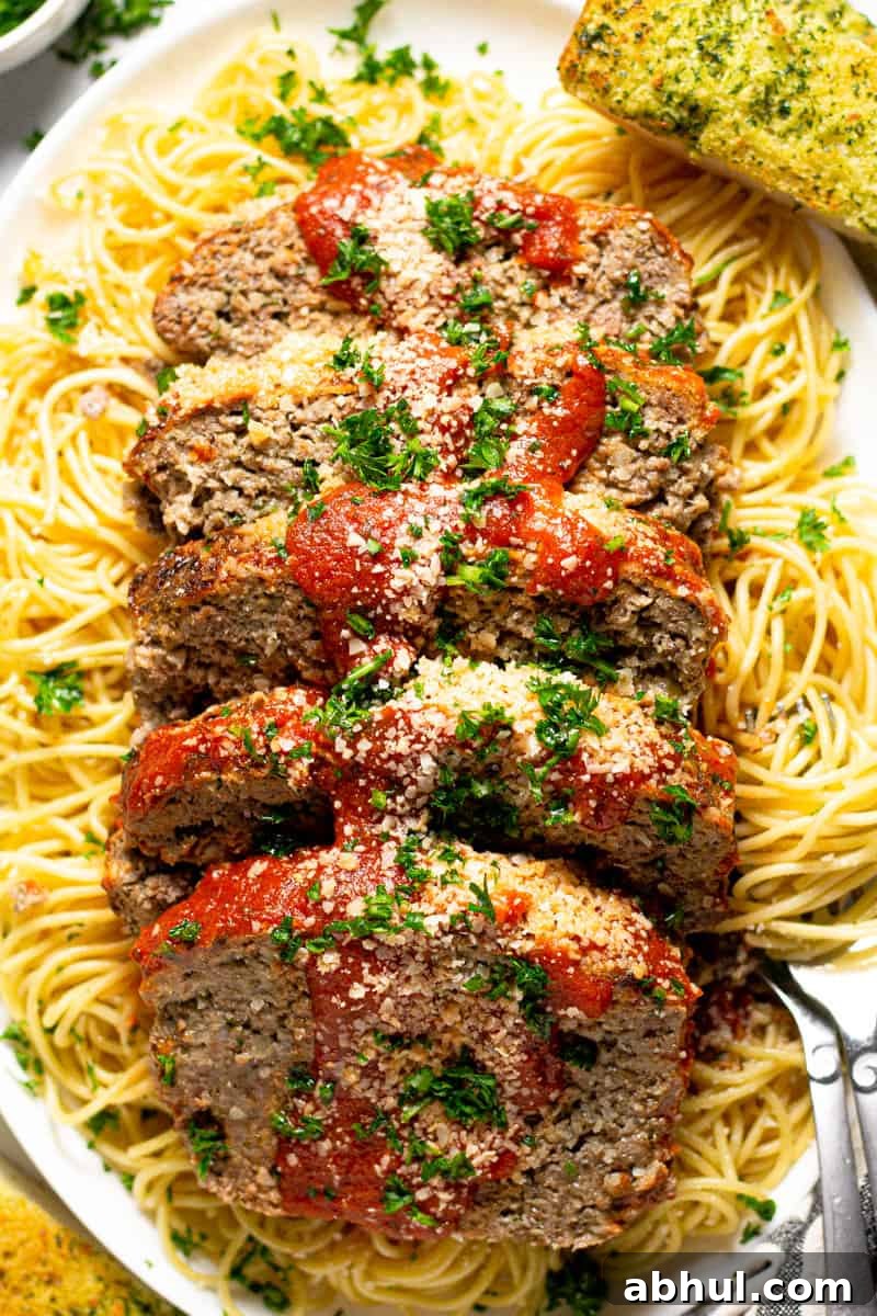 Large white platter with an Italian meatloaf sliced on top of a bed of spaghetti noodles 