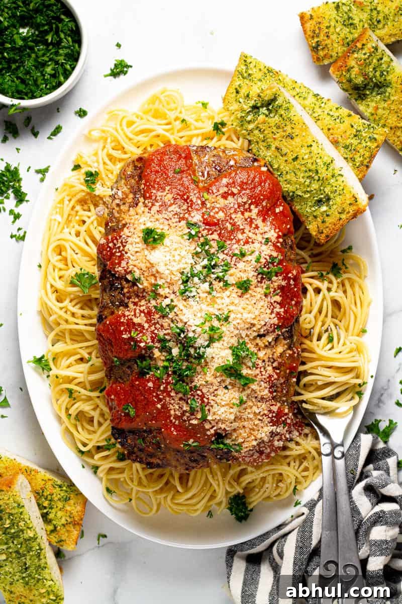 Large white platter with an Italian meatloaf sliced on top of a bed of spaghetti noodles 