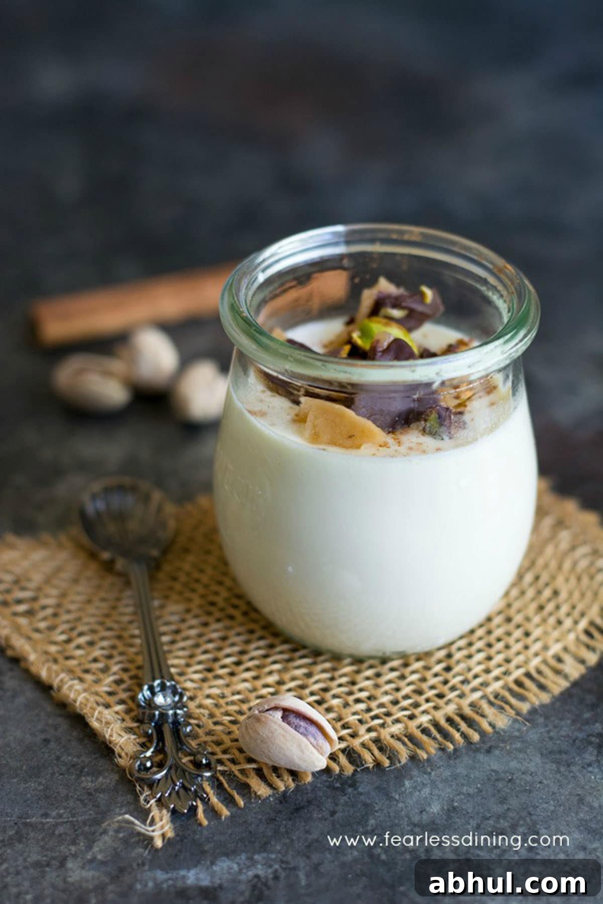 A fancy glass filled with eggnog panna cotta. It is garnished with crushed pistachio toffee.
