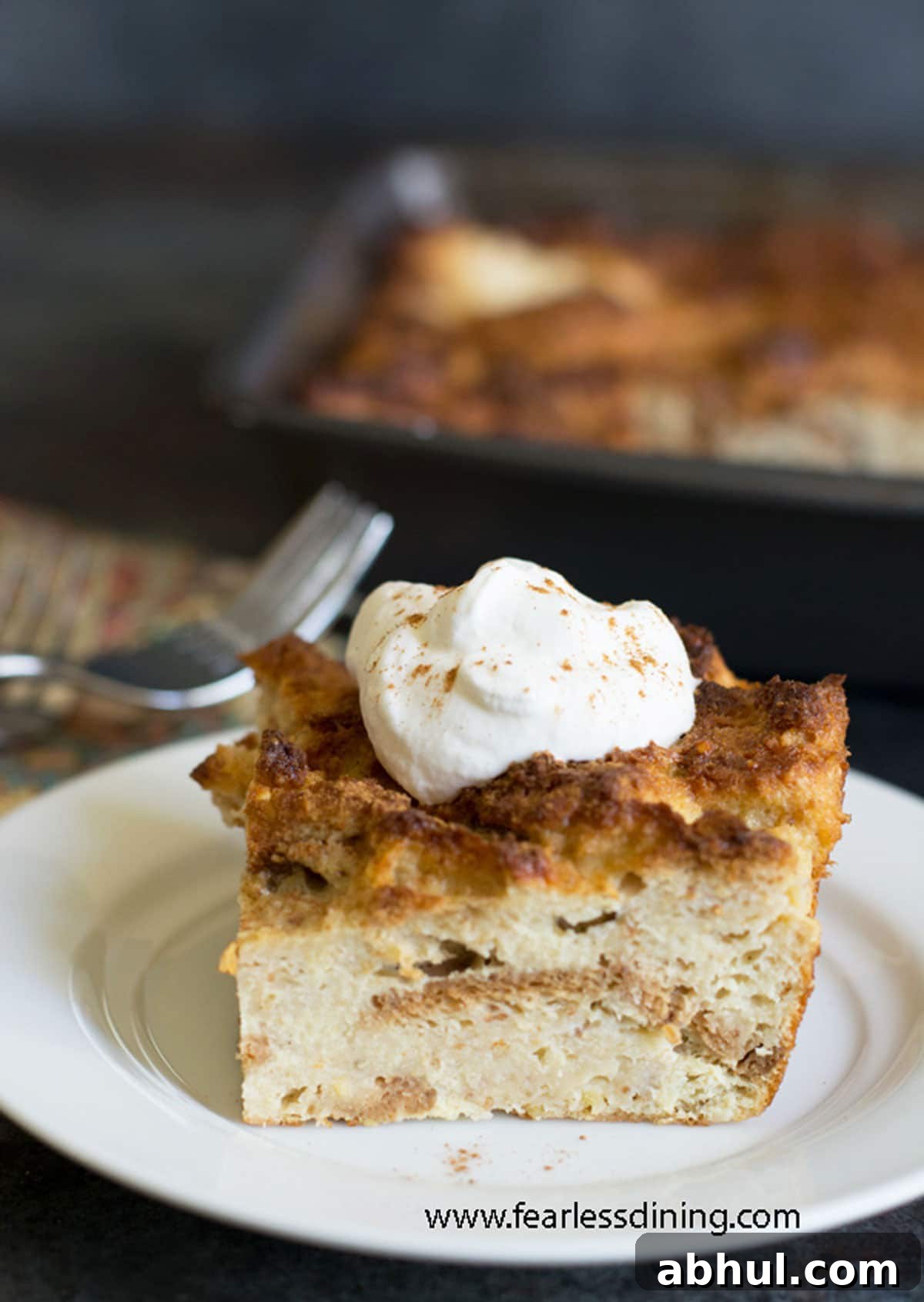 A slice of eggnog bread pudding on a plate. It has a small dollop of whipped cream.