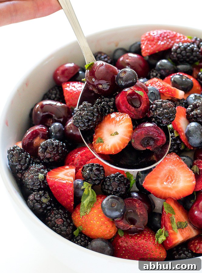 Spooning Berry Fruit Salad out of a large white bowl