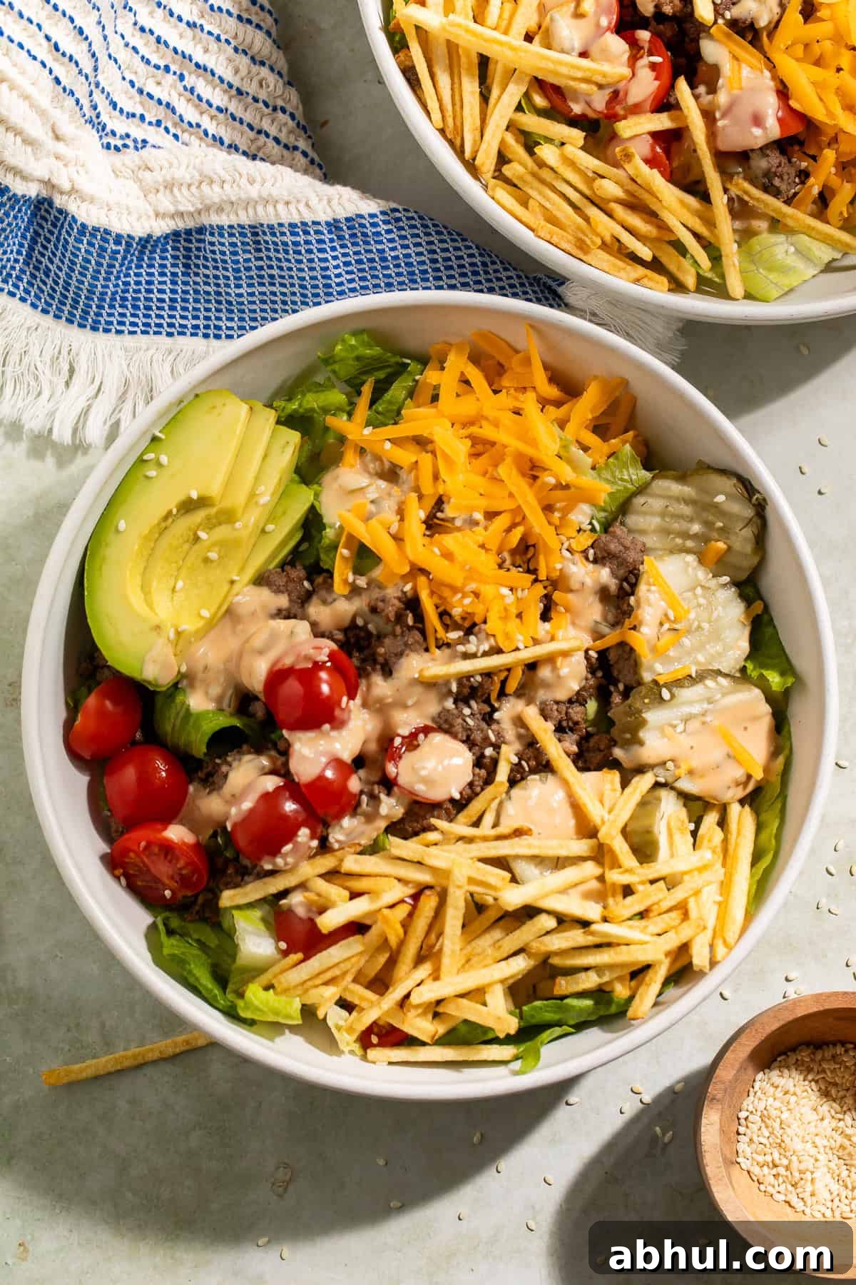 Close-up of a burger bowl with ground beef, cheddar cheese, avocado, pickles, tomatoes, and crispy potato sticks
