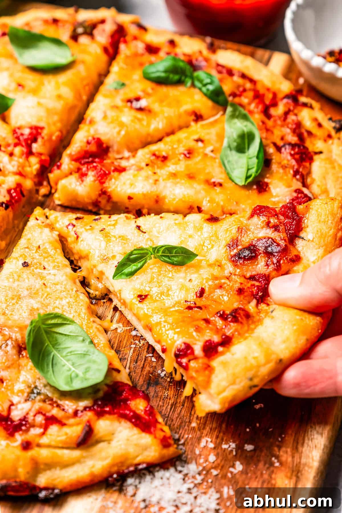 A hand lifting a slice of cottage cheese pizza from a wooden cutting board.