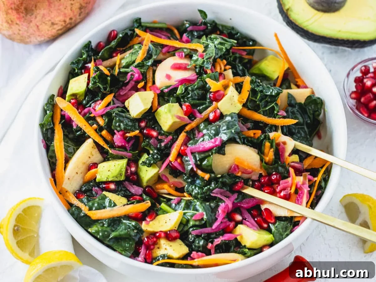 Kale salad in a white bowl with lemons and avocado on the side