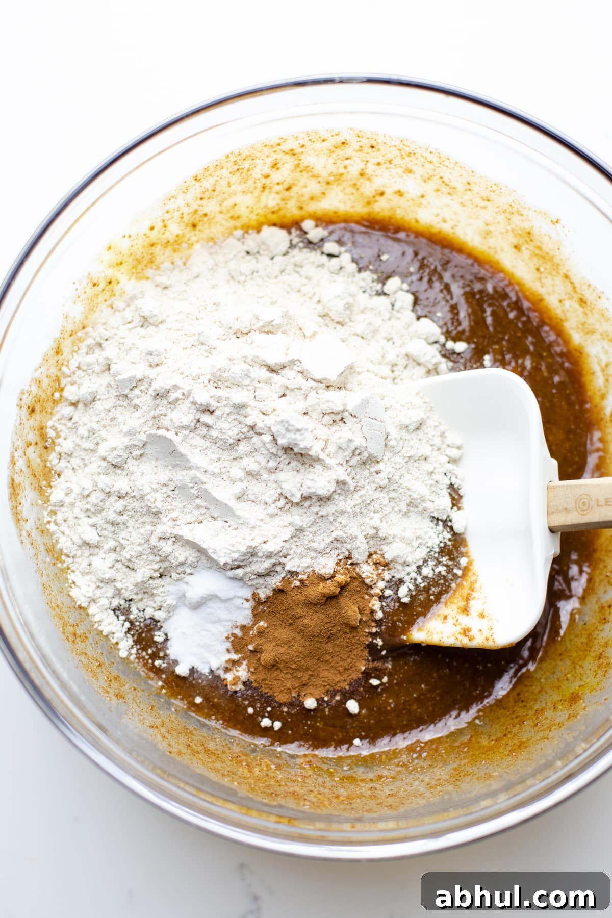 Mixing dry ingredients with wet ingredients in a clear bowl with a rubber spatula.