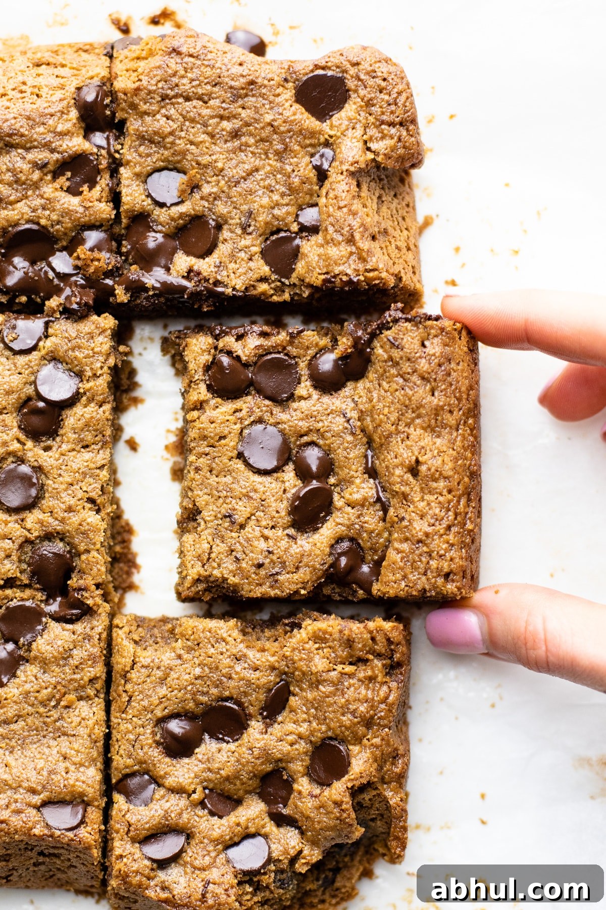 Two fingers picking up a peanut butter bar laying on parchment paper. 