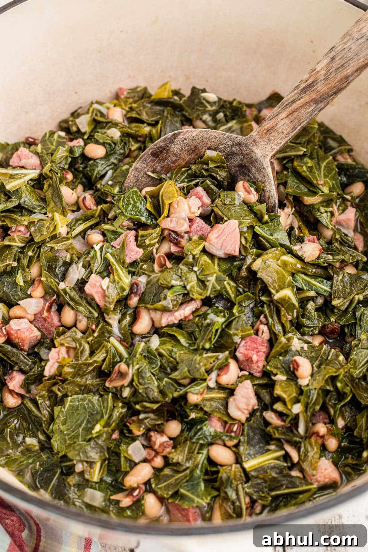 Closeup inside a pot with a spoon digging into the collard greens and black eyed peas.